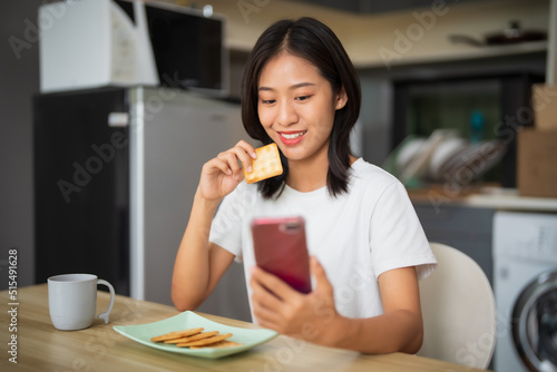 Asian girl using cell phone while drinking coffee at home in the morning