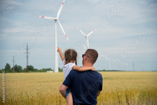 A girl and her dad look at the wind generator in the field. Ecology. Future.