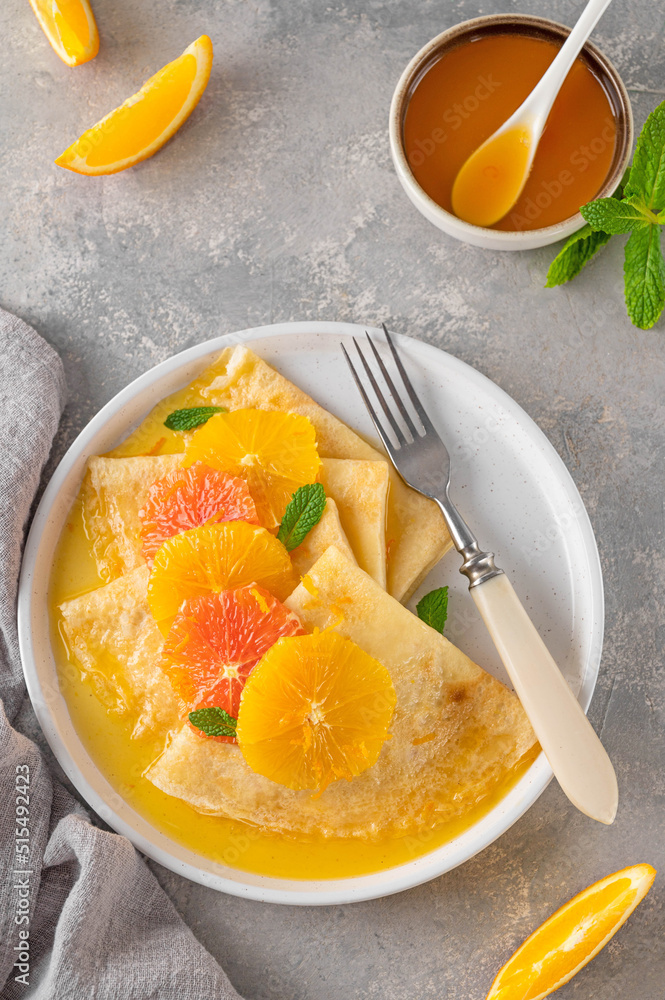 Delicious crepes suzette with orange syrup and slices fruits on a plate on a gray concrete background, top view Delicious crepes suzette with orange syrup and slices fruits on a plate on a gray concrete background, top view