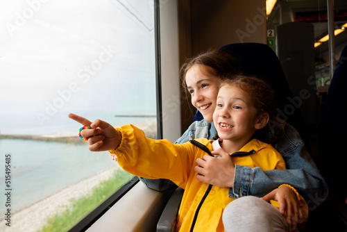 Two sister girls look out the window of a train at the sea.The girls are talking and having fun. Journey. Reflection. Vacation. Summer. Family vacation.