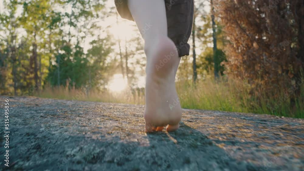 Barefoot legs of man walking through wild flowers and moss on sunny day. Man wears brown trousers walking on rock pathway against forest at back sunlight low angle shot Barefoot legs of man walking through wild flowers and moss on sunny day. Man wears brown trousers walking on rock pathway against forest at back sunlight low angle shot