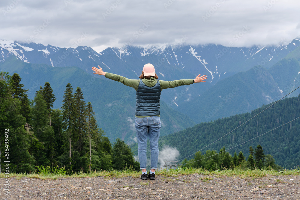 Happy girl with her arms outstretched enjoying the view of mountain peaks. Traveling and hiking concept.