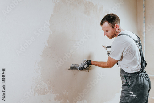 Builder in work overalls plastering a wall indoor