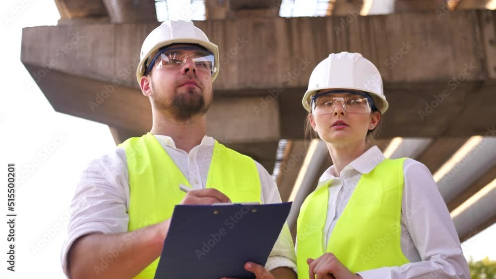 Two civil engineers, a young man and a young woman working on a project wearing safety helmets, are discussing real estate development and planning at a construction site together Two civil engineers, a young man and a young woman working on a project wearing safety helmets, are discussing real estate development and planning at a construction site together
