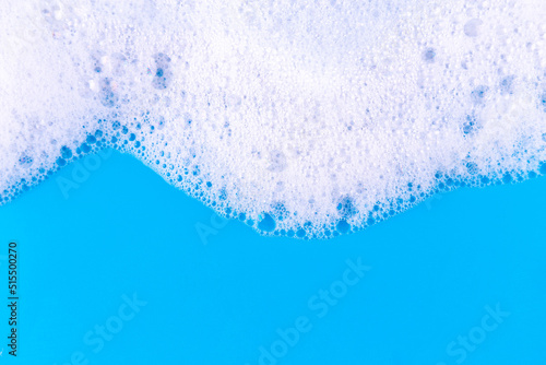 Foaming liquid on blue backdrop. Cosmetics foam background. Cosmetic product sample of mousse, shampoo or soap. Skincare, cosmetology and beauty concept