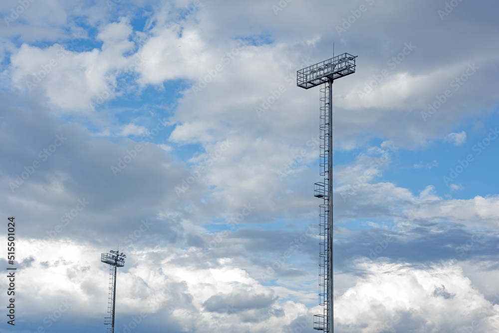 Metal high tower with lanterns in the stadium, sports lighting, spotlight against the blue sky Metal high tower with lanterns in the stadium, sports lighting, spotlight against the blue sky