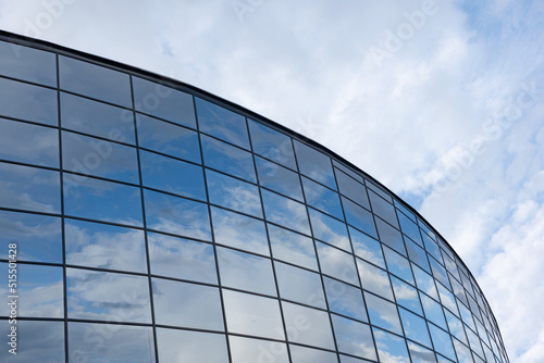 Mirrored windows of a modern building reflect the blue sky and clouds