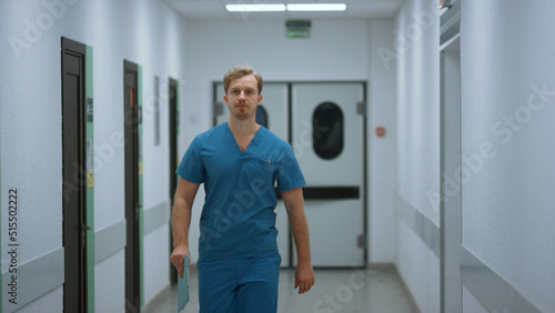 Serious doctor walking down hospital corridor. Medic going in clinic hallway.