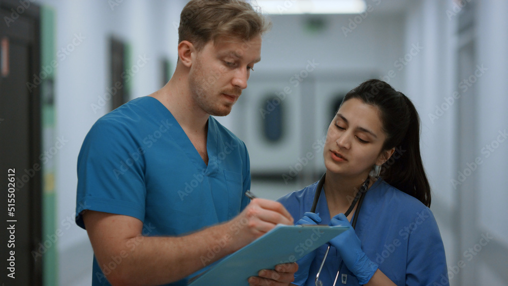 Surgeon discussing patient diagnosis with nurse standing clinic corridor closeup Surgeon discussing patient diagnosis with nurse standing clinic corridor closeup