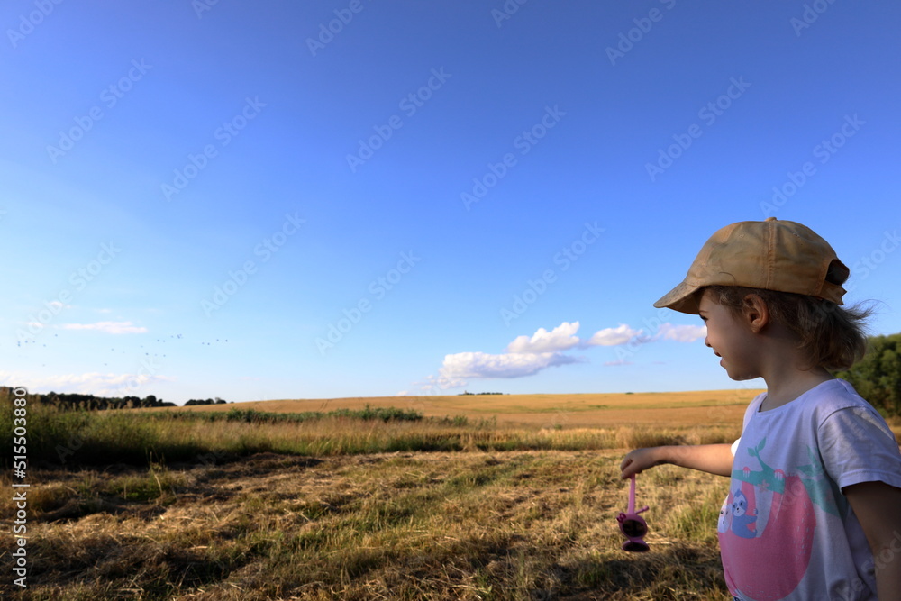 Child in the bosom of nature admires the landscape, a beautiful view of a wheat field on a background of the blue sky Child in the bosom of nature admires the landscape, a beautiful view of a wheat field on a background of the blue sky