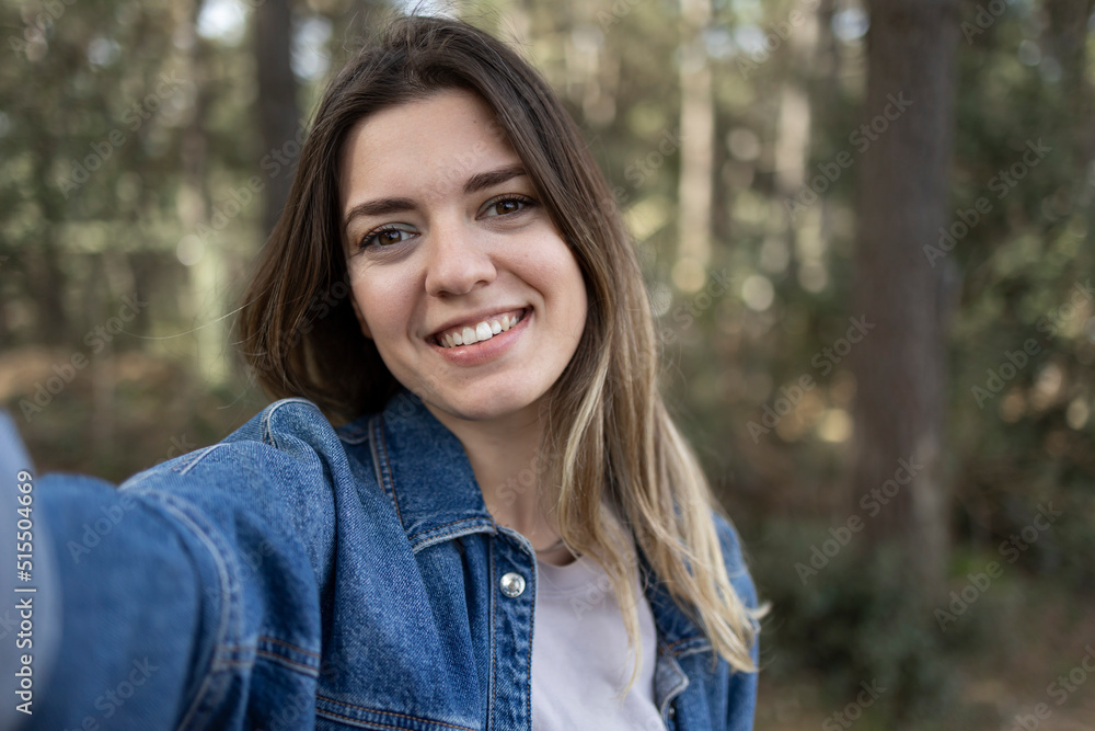 Happy young influencer woman taking selfie at forest. She will share on social media. She is smiling. Nature, travel, walking concept. Happy young influencer woman taking selfie at forest. She will share on social media. She is smiling. Nature, travel, walking concept.