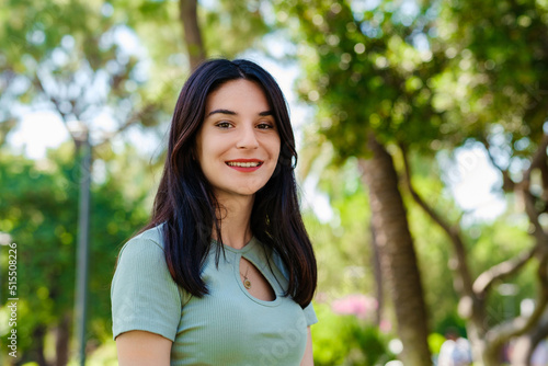 Brunette millennial woman wearing turquoise tee on city park, outdoors looking at camera while posing. Natural beauty concept. Beautiful girl. Pretty young woman.