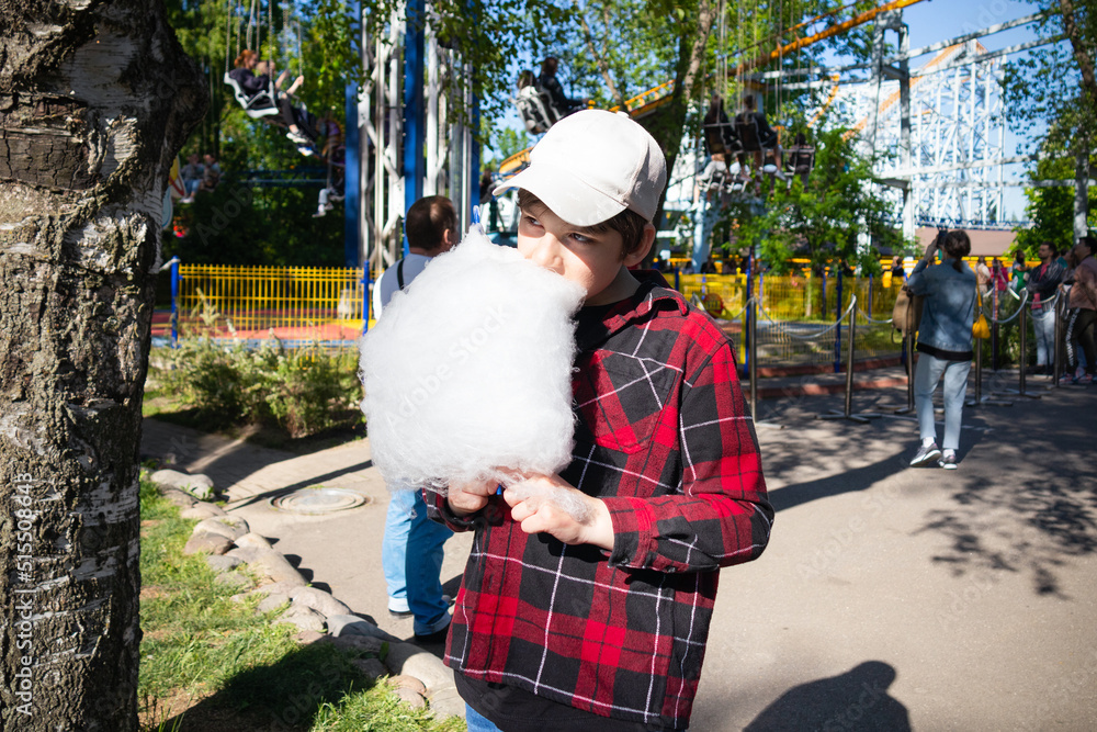 Boy eating white cotton candy in red checkered shirt and cap outdoor, summer day Boy eating white cotton candy in red checkered shirt and cap outdoor, summer day
