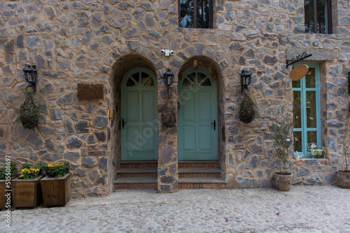 front facade of a medieval house with two wooden doors and two windows above in rock stone wall with security cameras in a medieval italian tuscany villa in Val'Quirico, Tlaxcala, Puebla, Mexico