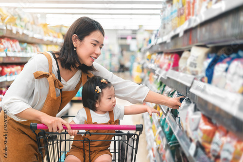 Asian mother and her daughter buying food at huge supermarket , Baby sit in trolley, Family shopping concept.