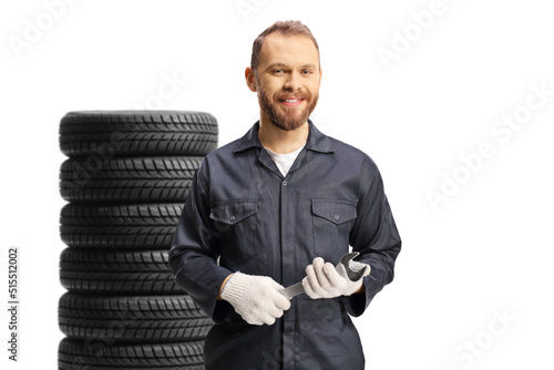 Smiling mechanic in a uniform with tires holding a wrench tool