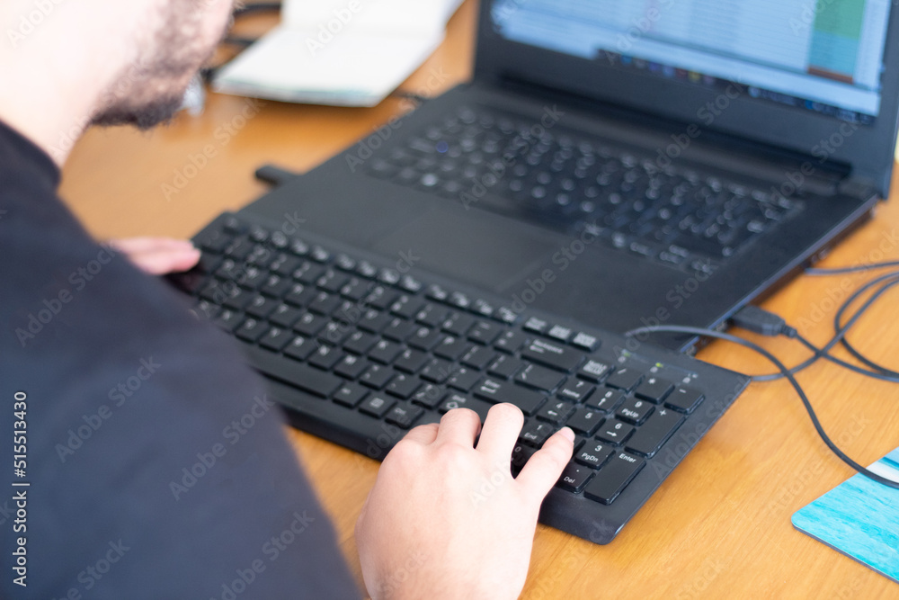 Unrecognizable man working in front of a laptop with an extra keyboard Unrecognizable man working in front of a laptop with an extra keyboard