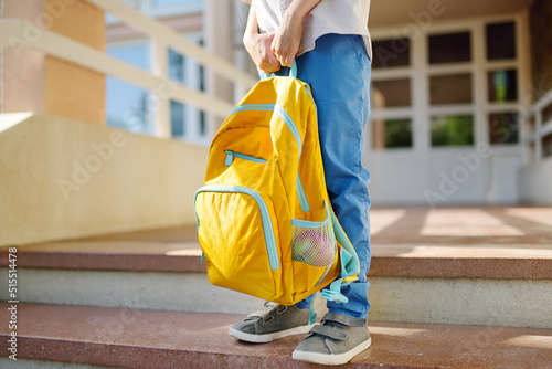 Little student with a backpack on the steps of the stairs of school building. Close-up of child legs, hands and schoolbag of boy standing on staircase of schoolhouse.Back to school concept. photo