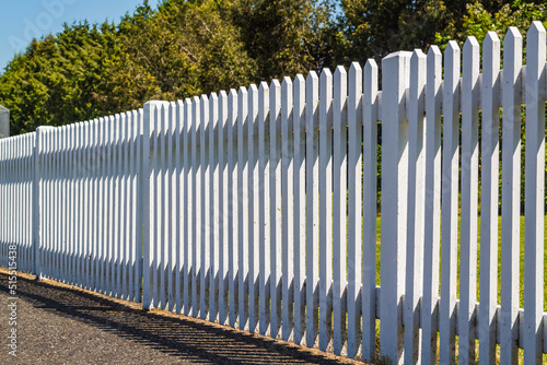 White wooden fence on the blue sky background. Green lawn and wooden white fence on sunny summer day