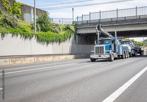 Towing semi truck with extended arrow transporting unexpectedly broken big rig semi truck with tip trailer running on the highway road