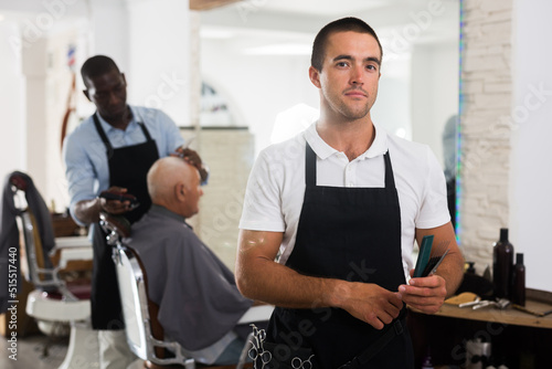 Portrait of successful professional young barber standing in hair salon..