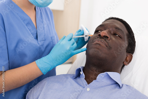 Afro american man getting procedure of injection for face skin tightening in aesthetic clinic