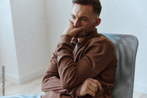 Upset frustrated thoughtful pensive serious young man reclines on hand looks aside think about divorce break up sitting in chair at home. People emotions Problems concept. Copy space photo