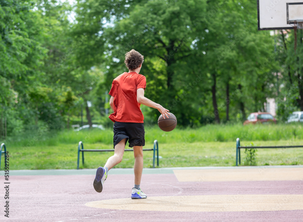 Teenager running in the stadium. Cute young teenager in red t shirt with a ball plays basketball on court. Sports, hobby, active lifestyle for boys	