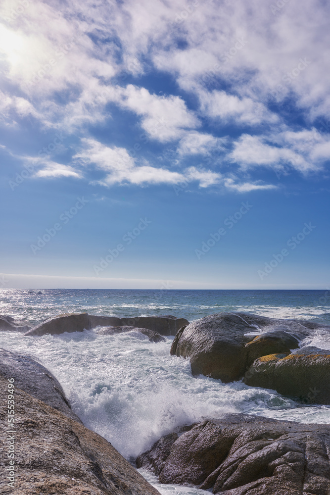 Rocks in the ocean under a blue cloudy sky with copy space. Scenic landscape of beach waves splashing against boulders or big stones in the sea at a popular summer location in Cape Town, South Africa