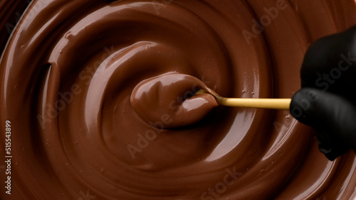 Hand stirring melted dark chocolate with golden spoon, close up. Liquid hot chocolate. Confectioner prepares chocolate dessert, glaze photo