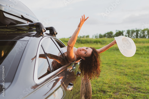 Beautiful young woman travels by car, leaning out the window and having fun photo