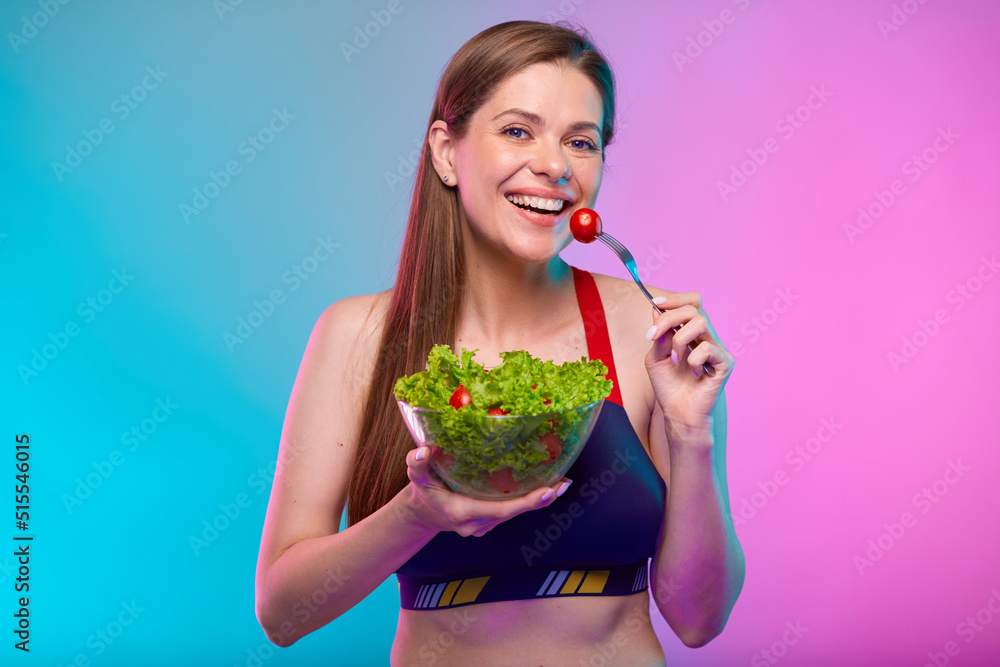 Smiling woman in sportswear eating green salad in glass bowl. Female fitness portrait isolated on neon multicolor background. Smiling woman in sportswear eating green salad in glass bowl. Female fitness portrait isolated on neon multicolor background.