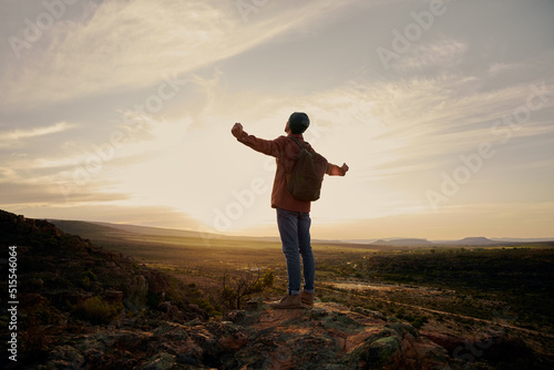 Young man with backpack standing on mountain with hands outstretched