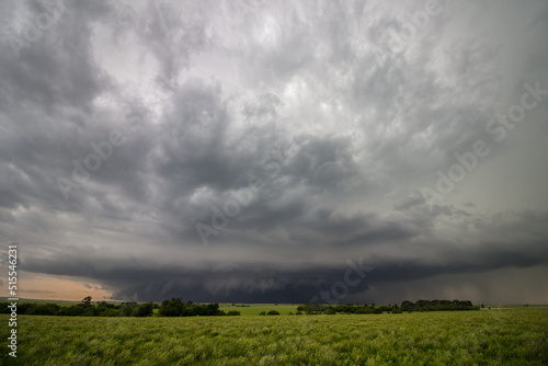 A strong thunderstorm looms on the horizon over a green field in Kansas.