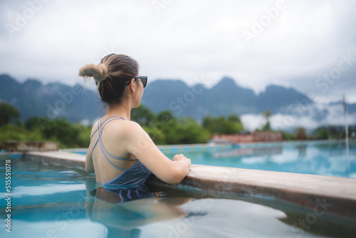 Young Asian woman having relaxation in swimming pool with nature mountain view, summer holiday vacation time for happy enjoy travel lifestyle in water outdoor at beauty resort with blue sky © chokniti
