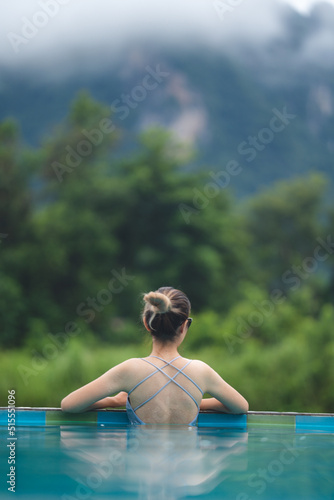 Young Asian woman having relaxation in swimming pool with nature mountain view, summer holiday vacation time for happy enjoy travel lifestyle in water outdoor at beauty resort with blue sky