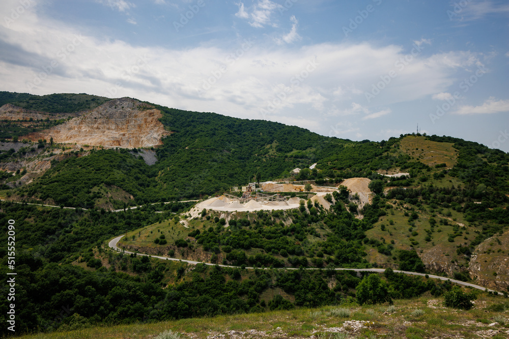 Quarry for extraction of minerals with equipment and machines, and road, in Rhodope Mountains covered with forests