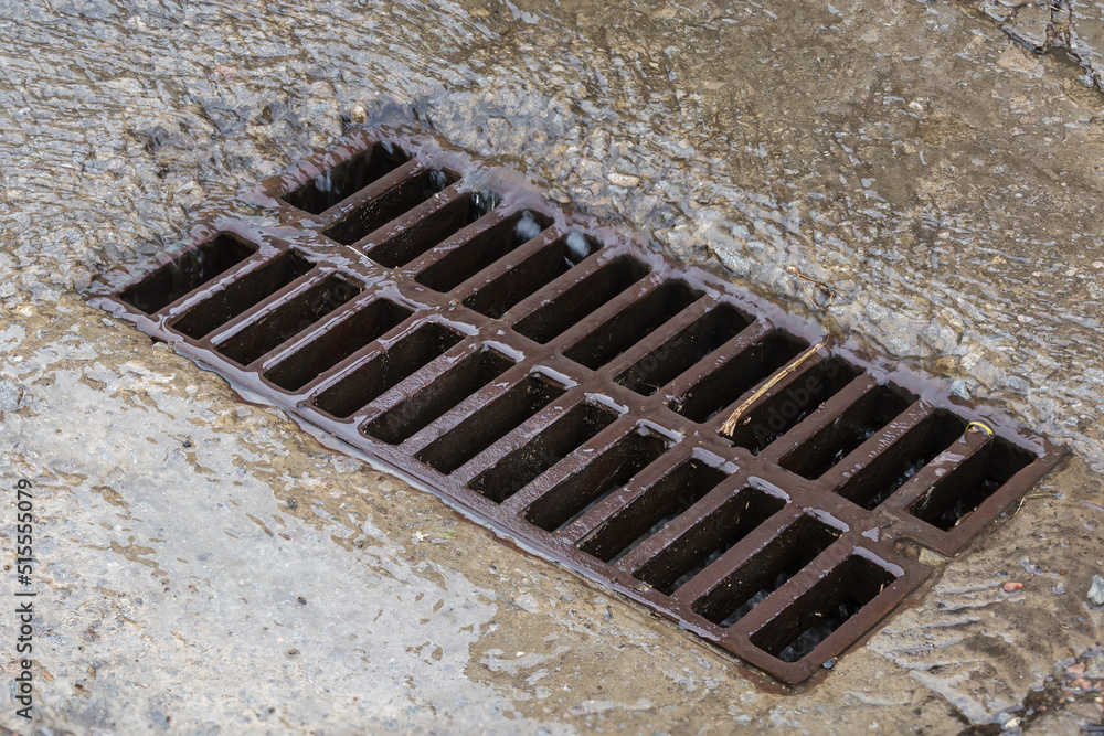Rainwater running down to storm drain with cast iron grid
