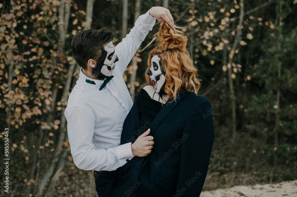 A couple in love is standing in the woods celebrating Halloween in costumes and makeup and laughing