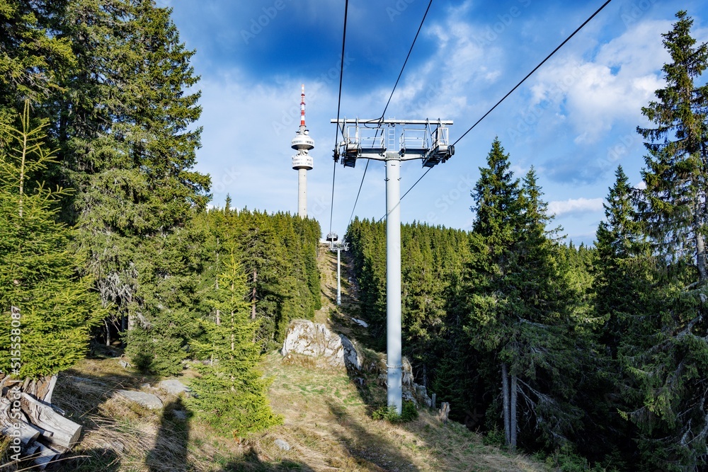 Lift with cable passes between spruce forest on peak against backdrop of mountain ranges of Rhodope Mountains