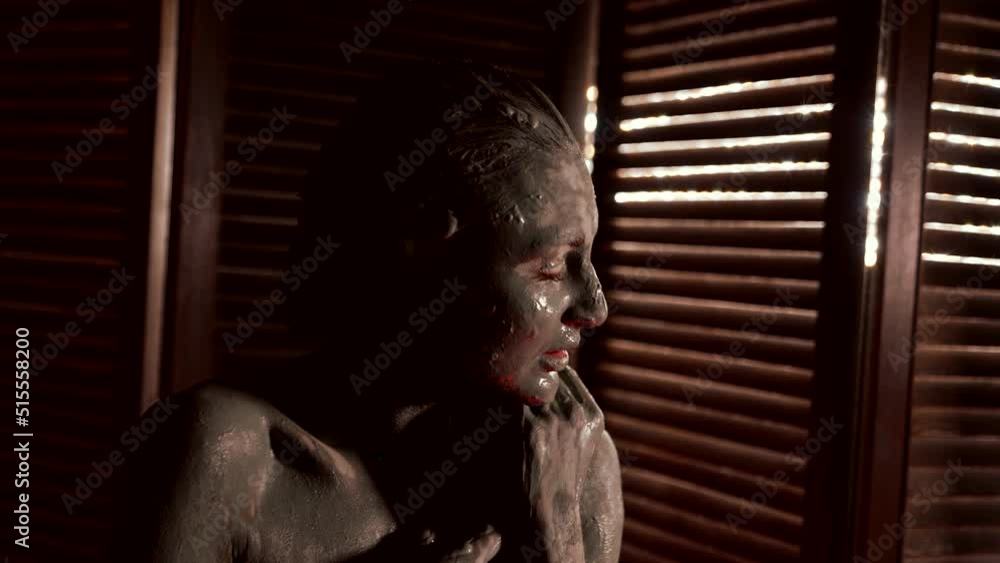 portrait of a woman smeared with clay on the background of wooden blinds. close-up portrait of a woman smeared with clay on the background of wooden blinds. close-up