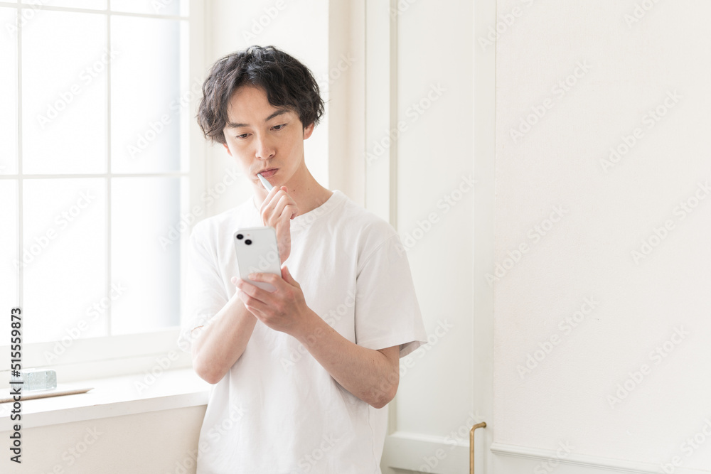 携帯電話を見ながら歯を磨く若い男性。 携帯電話を見ながら歯を磨く若い男性。