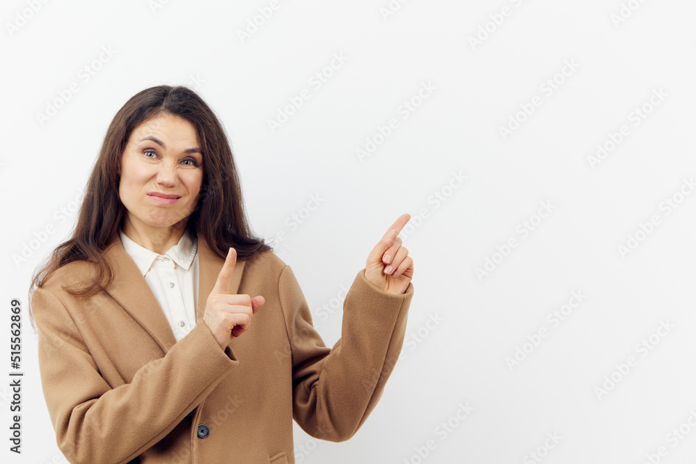 a beautiful, well-groomed, attractive woman with long dark hair stands on a light background, pointing with her hands at an empty area for an advertising insert a beautiful, well-groomed, attractive woman with long dark hair stands on a light background, pointing with her hands at an empty area for an advertising insert