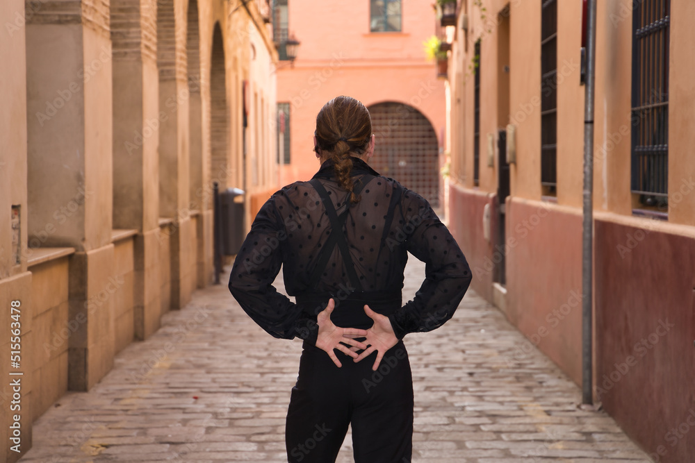Young man with beard and ponytail, wearing black transparent shirt with black polka dots, black pants and jacket, dancing flamenco in the city. Concept art, dance, culture, tradition. Young man with beard and ponytail, wearing black transparent shirt with black polka dots, black pants and jacket, dancing flamenco in the city. Concept art, dance, culture, tradition.