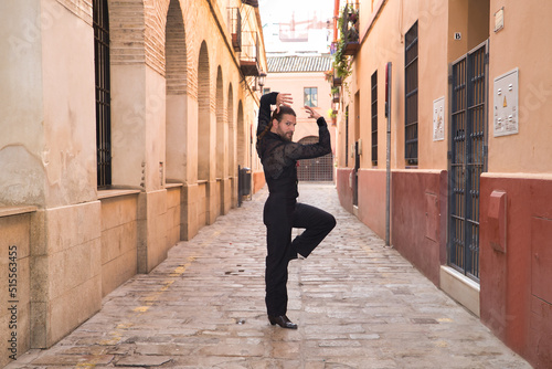 Young man with beard and ponytail, wearing black transparent shirt with black polka dots, black pants and jacket, dancing flamenco in the city. Concept art, dance, culture, tradition.