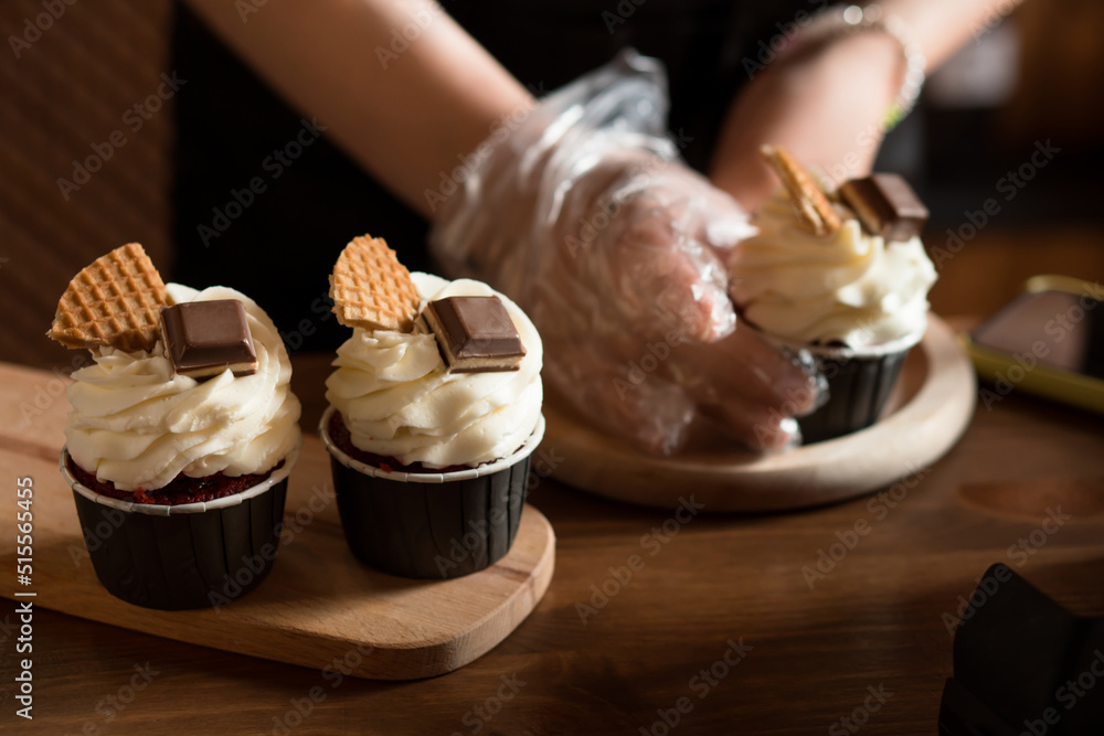 Hands of craftswoman baker making cupcakes with cheese cream, decorated by chocolate
