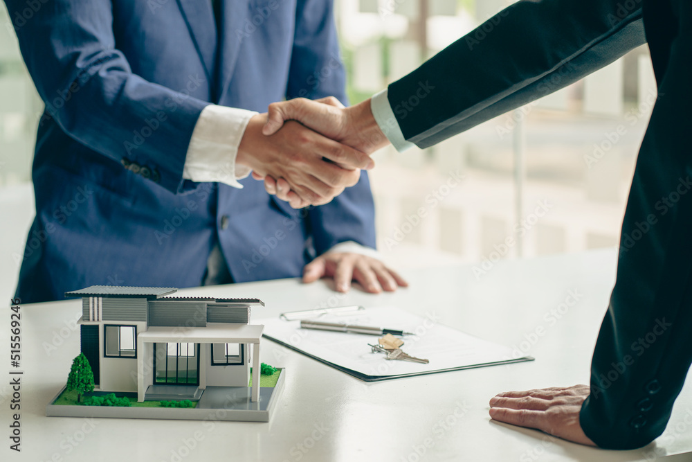 Sales agents and landlords when signing a contract to buy or rent a new home. Real estate agents shake hands with customers after signing contracts. Contract documents and house plans on a wooden tabl