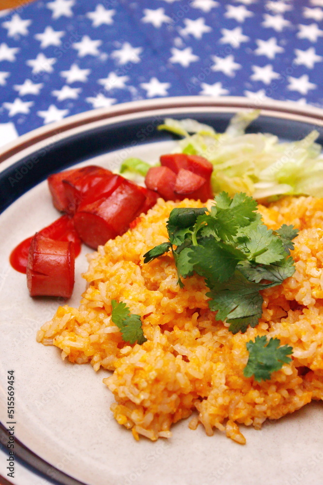 Fried rice with tomato sauce served in a white plate with fillings and sautéed tomatoes on an American flag-themed table. Fried rice with tomato sauce served in a white plate with fillings and sautéed tomatoes on an American flag-themed table.