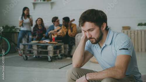 Young student guy feels upset and isolated while his friends celebrating party at home photo