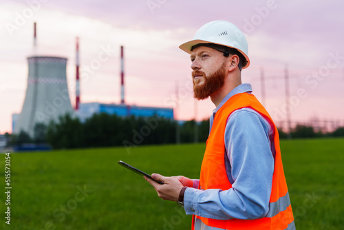 An engineer with a tablet on the background of a power plant. Inspection of engineering systems. A man in a helmet and an orange vest © makedonski2015